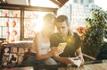 Young man and girl sitting on terrace at restaurant and using smartphone on sunset background, girl smiling, guy looking surprised Royalty Free Stock Photo
