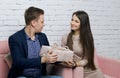 A young man gives a gift to a girl. He hands her a box of wrapping paper tied with a ribbon. Sitting on a sofa against a white Royalty Free Stock Photo