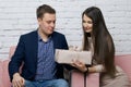 A young man gives a gift to a girl. She hands her a box of wrapping paper tied with a ribbon. Sitting on a sofa against a white Royalty Free Stock Photo