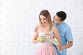 Young man giving present and flowers to his beloved girlfriend near white brick wall