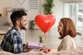 Young man giving present to his beloved girlfriend at home. Celebration of Saint Valentine's Day