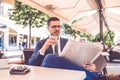 Young man with glass of water in hand reading newspaper at outdoor cafe Royalty Free Stock Photo