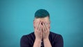 A young man in glasses with blue hair cries. Emotional man crying on a blue background.