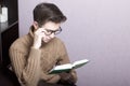 A young man with glasses reflects on an open book. Hand holding glasses for the bow. Thoughtful reading