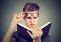 Young man with glasses suffering from eyestrain reading a book having vision problems