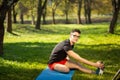 Young man in glasses training yoga outdoors. Sporty guy makes relaxing exercise on a blue yoga mat, in park. Copy space