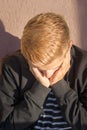 Young man with golden blond hair stands with his face hidden in the palms in the morning sun