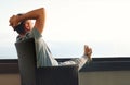 Young man in gray casual clothes sits on wicker chair and put his hands behind his head