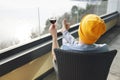 Young man in gray casual clothes and yellow hat sits on wicker chair and holds glass of red wine. Human is on huge balcony with