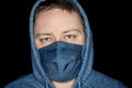 Portrait of a young man in a gray hoodie and in a gray cloth mask on a black background Royalty Free Stock Photo