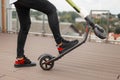 Young man in gray jeans in sneakers posing with an electric scooter on a summer terrace. Closeup of male legs on a modern scooter Royalty Free Stock Photo