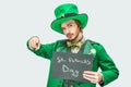 Young man in green suit holding dark tablet with St. Patrick`s writing on it. He point straight and look on camera