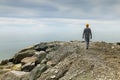 A young man in grey casual clothes and a yellow hat walks along at the empty rocky seashore. Lonely walk by the sea