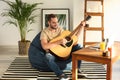 Young man with guitar sitting on beanbag chair at home Royalty Free Stock Photo