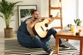 Young man with guitar sitting on beanbag chair at home Royalty Free Stock Photo