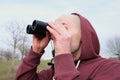 Young man, a guy stalker in a hood looks through black binoculars, peeps, hunts down secrets, the concept of surveillance, Royalty Free Stock Photo