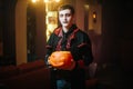 Young man in a Halloween costume of Count Dracula raises a carved pumpkin