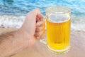 Young man hand holding a refreshing beer on the beach with wave