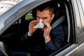 Young man with handkerchief. Sick guy has runny nose. Male model makes a cure for the common cold in the car. Royalty Free Stock Photo