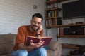 Young man has found an interesting old book in an antique shop and is happily reading it at home while sitting on the sofa in his Royalty Free Stock Photo