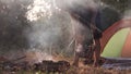 A young man is grilling meat on a fire in the forest.