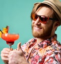 Young man in hat show thumb up drinking red margarita cocktail drink juice happy looking at camera over blue Royalty Free Stock Photo