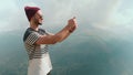 A young man in a hat and sunglasses, standing against the background of mountains and photographing beautiful landscapes Royalty Free Stock Photo