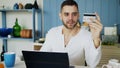 Young man having online shopping using credit card and laptop computer while have breakfast in the kitchen at home Royalty Free Stock Photo