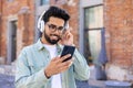 A young man in headphones is walking around the city, joyful, smiling, listening to music online, using an application Royalty Free Stock Photo