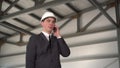 A young man in a helmet speaks on the phone at a construction site. The boss in a suit is talking on the phone.