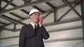 A young man in a helmet speaks on a walkie-talkie at a construction site. The boss in the suit looks around.