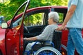 Young man helping disabled senior woman in wheelchair to get into car Royalty Free Stock Photo