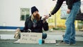 Young man helps to homeless person and giving him some food while beggar drink alcohol and sit near shopping cart at