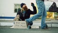 Young man helps to homeless person and giving him some money while beggar drink alcohol and sit near shopping cart at Royalty Free Stock Photo