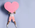 Young man hide his face behind pink heart shape toy in hands on pastel purple wall background Royalty Free Stock Photo