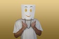 Young man hiding face behind paper bag with drawn emoticon on light background Royalty Free Stock Photo