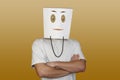 Young man hiding face behind paper bag with drawn emoticon on light background Royalty Free Stock Photo