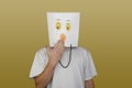 Young man hiding face behind paper bag with drawn emoticon on light background Royalty Free Stock Photo