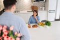 The young man is hiding flowers behind their backs to his girlfriend at home