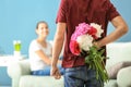 Young man hiding flowers for girlfriend behind his back indoors