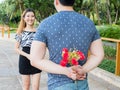 Young man hiding roses from his back and give them to his girlfriend.