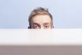 Young man is hiding. Squinted eyes behind the table. Spying. Voyeurism. Royalty Free Stock Photo