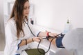 Young man with high blood pressure. Female doctor using sphygmomanometer with stethoscope checking blood pressure to a Royalty Free Stock Photo