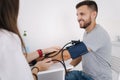 Young man with high blood pressure. Female doctor using sphygmomanometer with stethoscope checking blood pressure to a Royalty Free Stock Photo