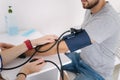 Young man with high blood pressure. Female doctor using sphygmomanometer with stethoscope checking blood pressure to a Royalty Free Stock Photo