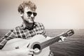 Young man hipster playing guitar by sea ocean. Royalty Free Stock Photo