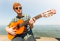 Young man hipster playing guitar by sea ocean. Royalty Free Stock Photo