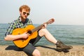 Young man hipster playing guitar by sea ocean. Royalty Free Stock Photo