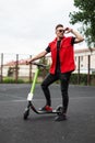 Young man hipster with a stylish hairstyle in trendy summer denim clothes stands with a vintage scooter and straightens sunglasses Royalty Free Stock Photo