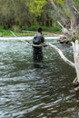 Young man on his back in a river or stream with rubber fishing boots and camouflage suit, backpack and tools for the sport of